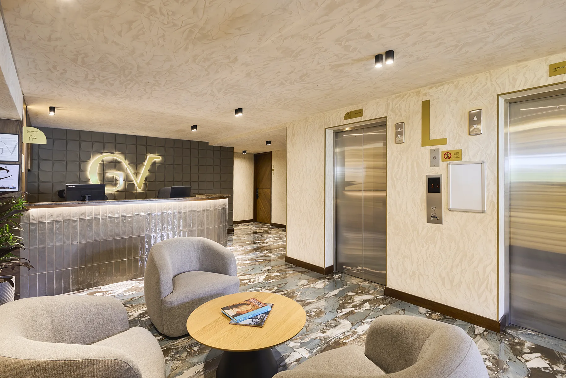 Lobby de Golden Valley Hotel con sillones color arena, mármol veteado y el monograma GV